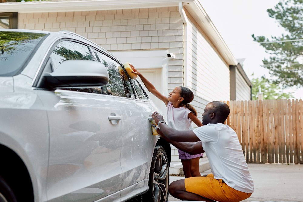 father and daughter washing car with outdoor camera in the background