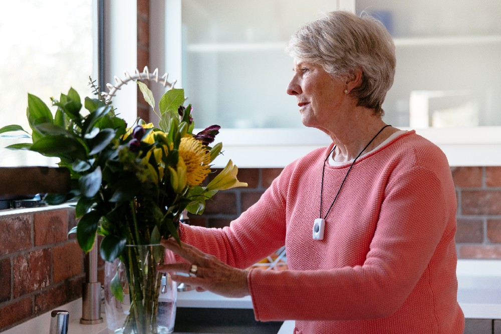 woman with emergency pendant at sink with flowers